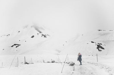 Rear view of person walking on snowcapped mountain against clear sky
