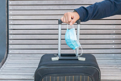 Cropped hand of man holding mask and suitcase
