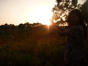 Woman standing on field against sky during sunset