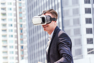 Smiling businessman gesturing while wearing virtual reality in city