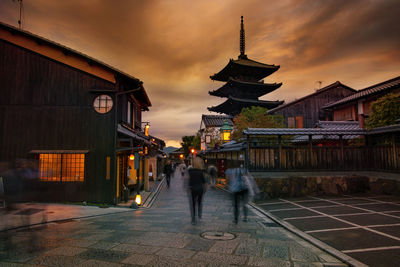 People walking on street amidst buildings in city during sunset