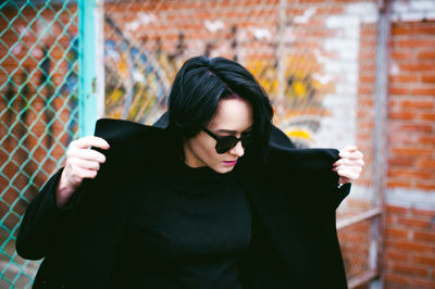 Young woman in sunglasses standing against chainlink fence