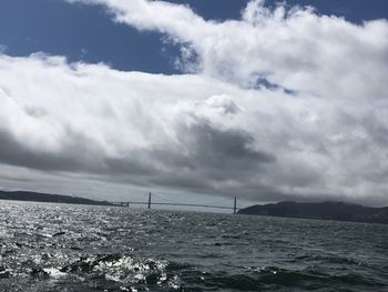 View of suspension bridge over sea against cloudy sky