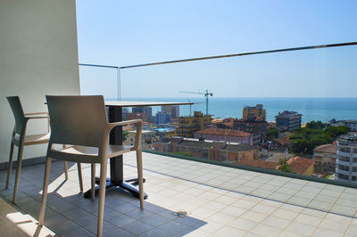 Chairs by sea against clear sky in city