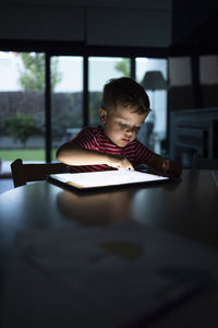 Boy using digital tablet while sitting at table in home