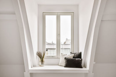 Soft cushions placed on white windowsill with decorative dried plants in glass vase near window in light room at home