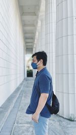 Side view of young man standing against building