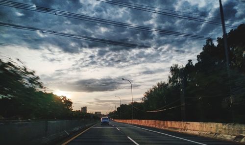 Road by trees against sky in city