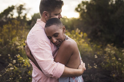 Side view of romantic couple embracing against plants in park during sunset