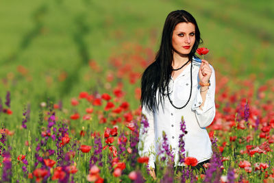 Beautiful young woman standing by poppy flowers in field