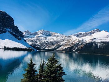 Scenic view of lake by snowcapped mountains against blue sky