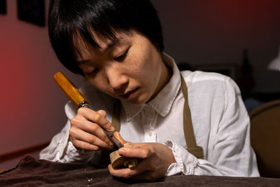 Young chinese female violin maker working with gouge to making a new violin in her workshop