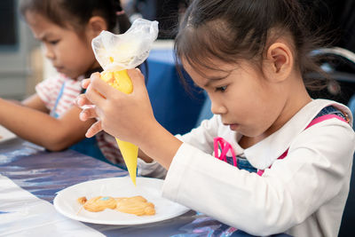 Cute girl decorating cookie with icing in plate on table