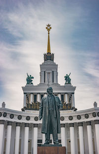 Low angle view of statue by building against cloudy sky