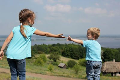 Sibling reaching towards each other against landscape