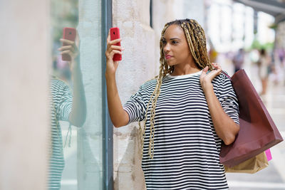 Woman holding shopping bags taking selfie through smart phone