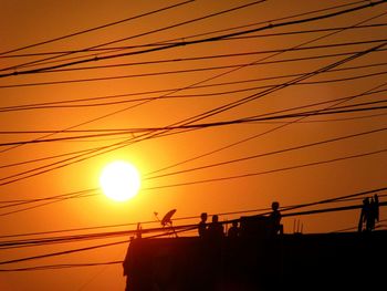 Low angle view of silhouette power lines against sky during sunset