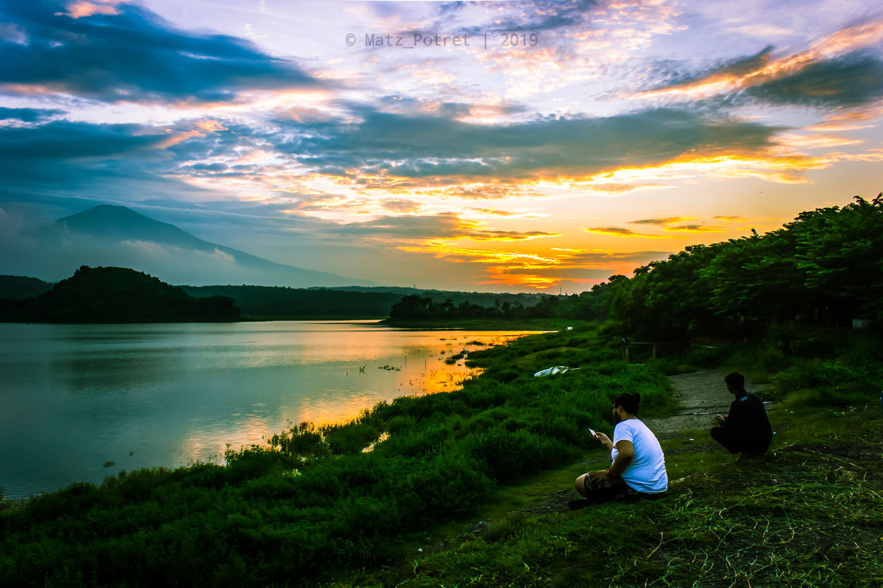 PEOPLE AT LAKE AGAINST SKY DURING SUNSET