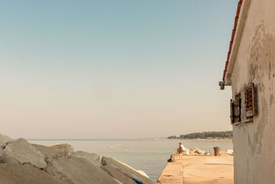 Distant view of man fishing at sea while sitting at harbor against sky