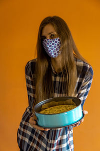 Portrait of young woman wearing mask against orange background