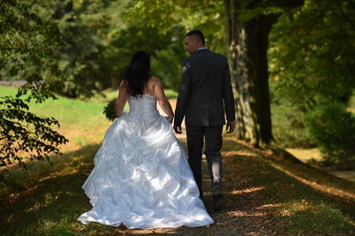 Rear view of newly wed couple walking on field in park