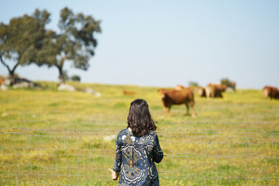 Rear view of woman standing by fence against sky