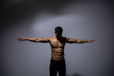 Rear view of shirtless man standing against gray background