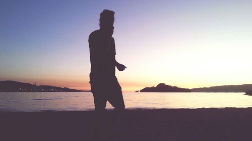 Silhouette man by sea against clear sky during sunset