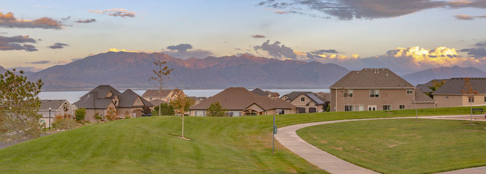 Houses on field by buildings against sky during sunset