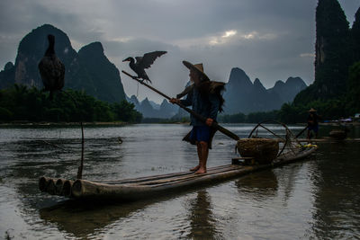 Man with birds on wooden rafts in lake against mountains