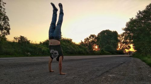 Full length of man doing handstand on road during sunset