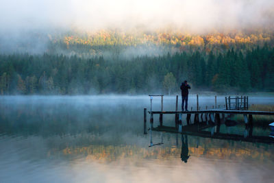 Rear view of man standing on pier over lake in foggy weather