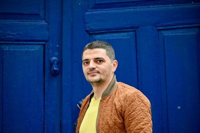 Portrait of young man standing against blue door