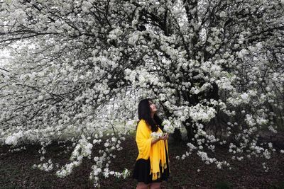 Side view of smiling young woman standing by flowering tree