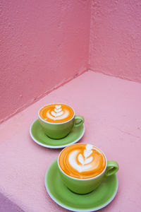 High angle view of two green cup of cappuccino on pink table