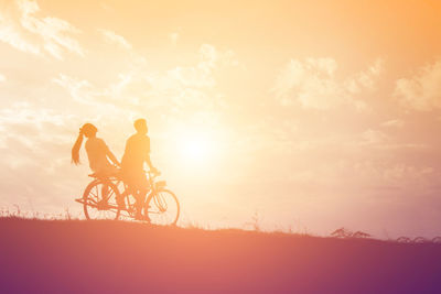 Silhouette people riding bicycle against sky during sunset