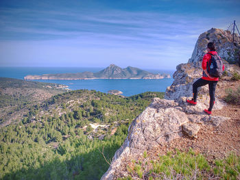 Sporty woman with backpack on rock view point in mallorka island mountains. rear view of middle-aged