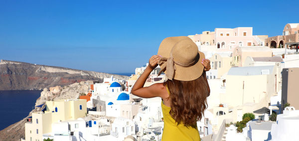 Rear view of woman standing against buildings at oia in santorini