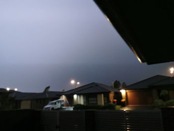 Illuminated street light by building against sky at night