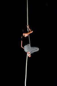 Low angle view of woman hanging on rope against black background