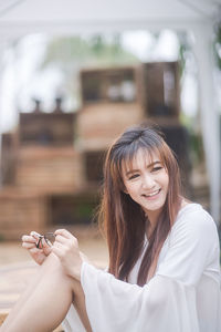 Cheerful young woman holding eyeglasses while sitting at home