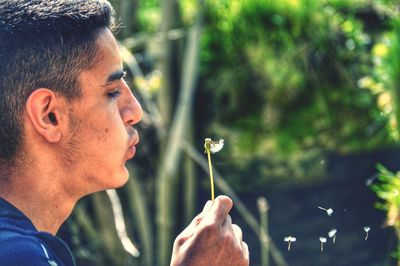 Close-up of man blowing dandelion against tree
