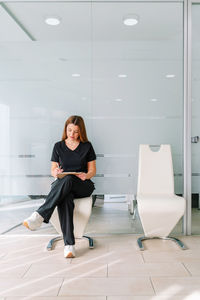 Pensive female worker with long hair in black outfit sitting and writing notes in documents in clipboard in modern clinic