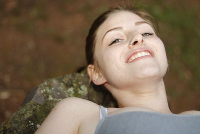 High angle portrait of smiling beautiful woman relaxing on rock at park