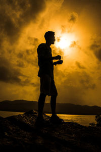 Silhouette man standing by sea against sky during sunset
