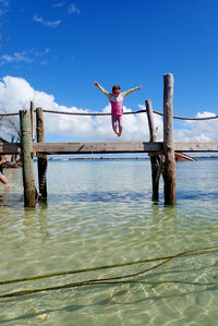 Woman jumping on wood against sky