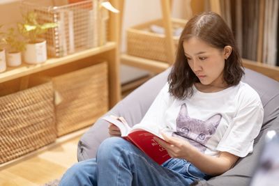 Girl looking away while sitting on book at home