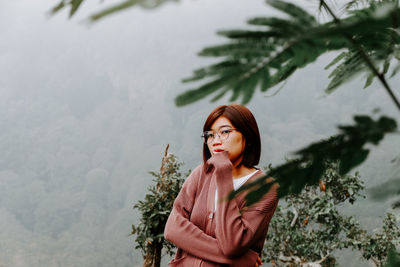 Portrait of young woman standing against tree