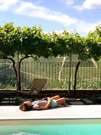 Woman lying in swimming pool against sky