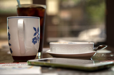 Close-up of bowl and coffee cup with mobile phone on table